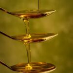 Artistic capture of honey pouring over stacked spoons with a green background.